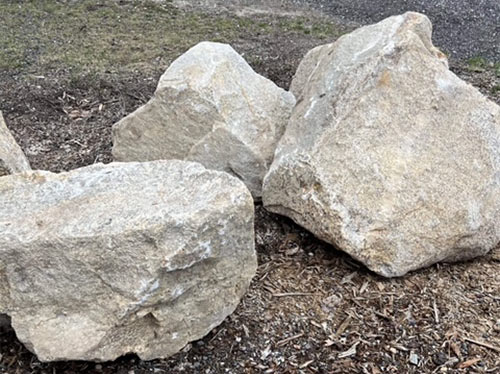 Three large boulders atop mulch in a landscape