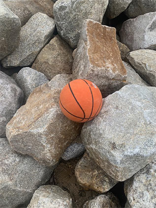A basketball in a pile of boulders to illustrate boulder size