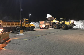 Snow removal equipment removing snow at night from a parking lot